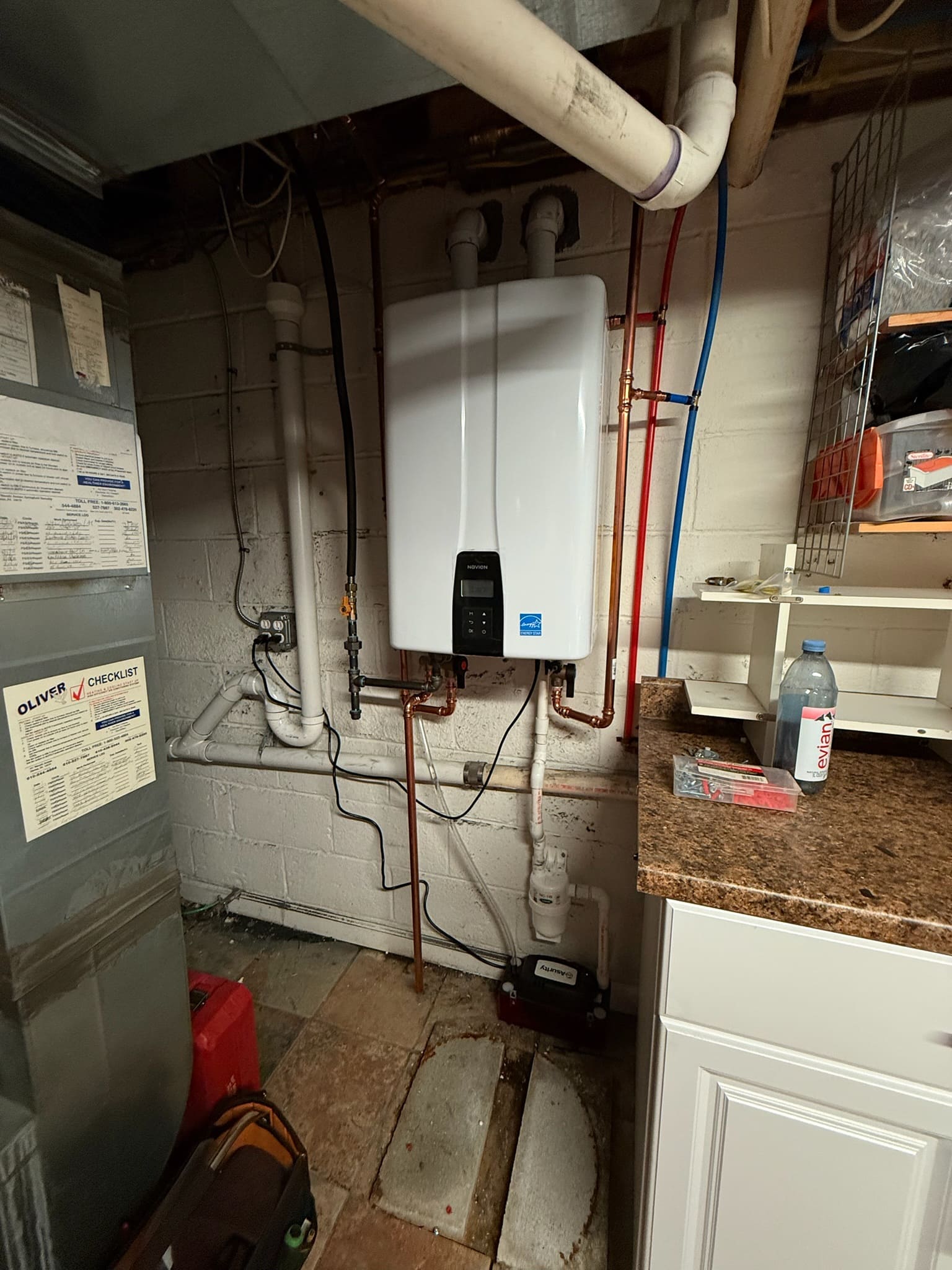 Indoor tankless water heater and connected piping Navien tankless water heater installed in a basement with exposed water pipes and overhead venting